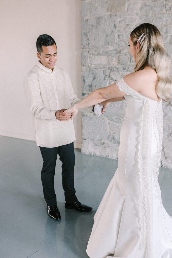 Groom takes his bride by the hands and admires her dress during their first look wedding photos at Bonsecours Market