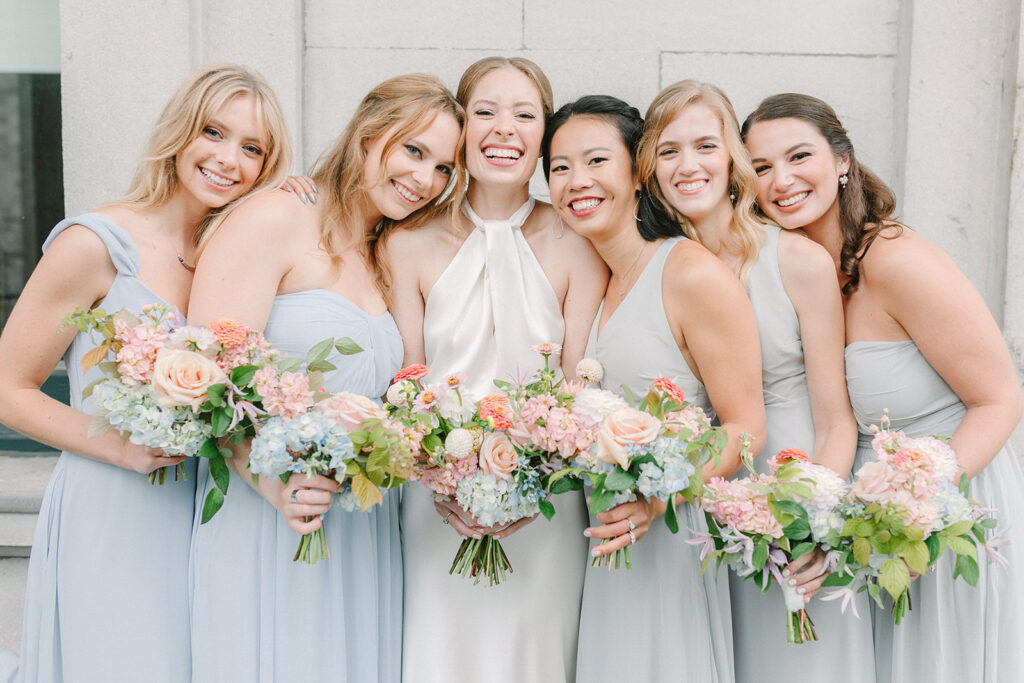 A bridge flashes a bright smile as she stands amongst her bridesmaids in their light blue dresses during her restaurant le richemond wedding