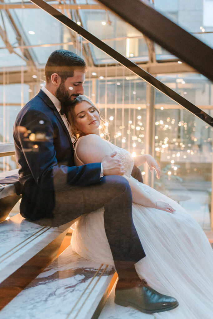 Beautiful bride leans back on her husband on marble steps at their William Gray Hotel wedding to take some photos