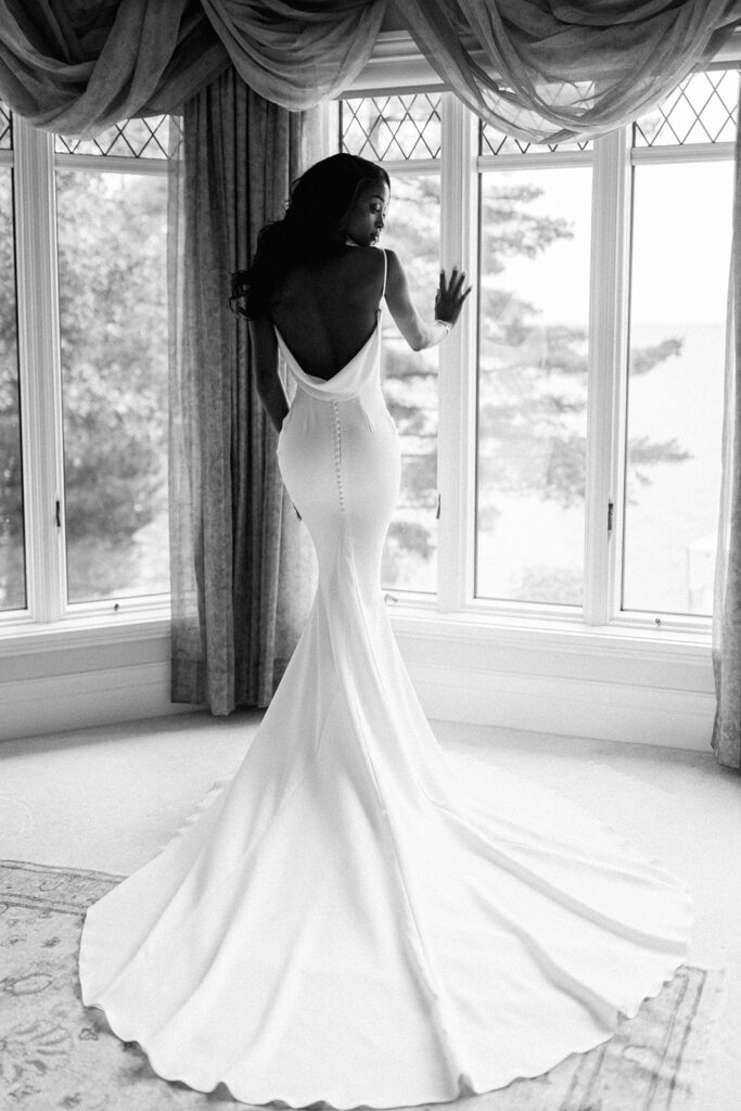 A bride confidently shows of the back of her dress to her professional wedding photographer in Montreal