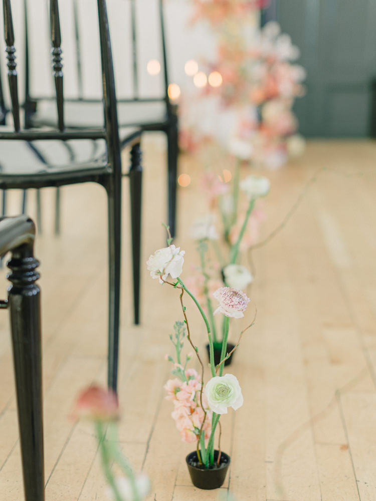 Delicate potted plants decorate the rows of a young couple's wedding ceremony seating area