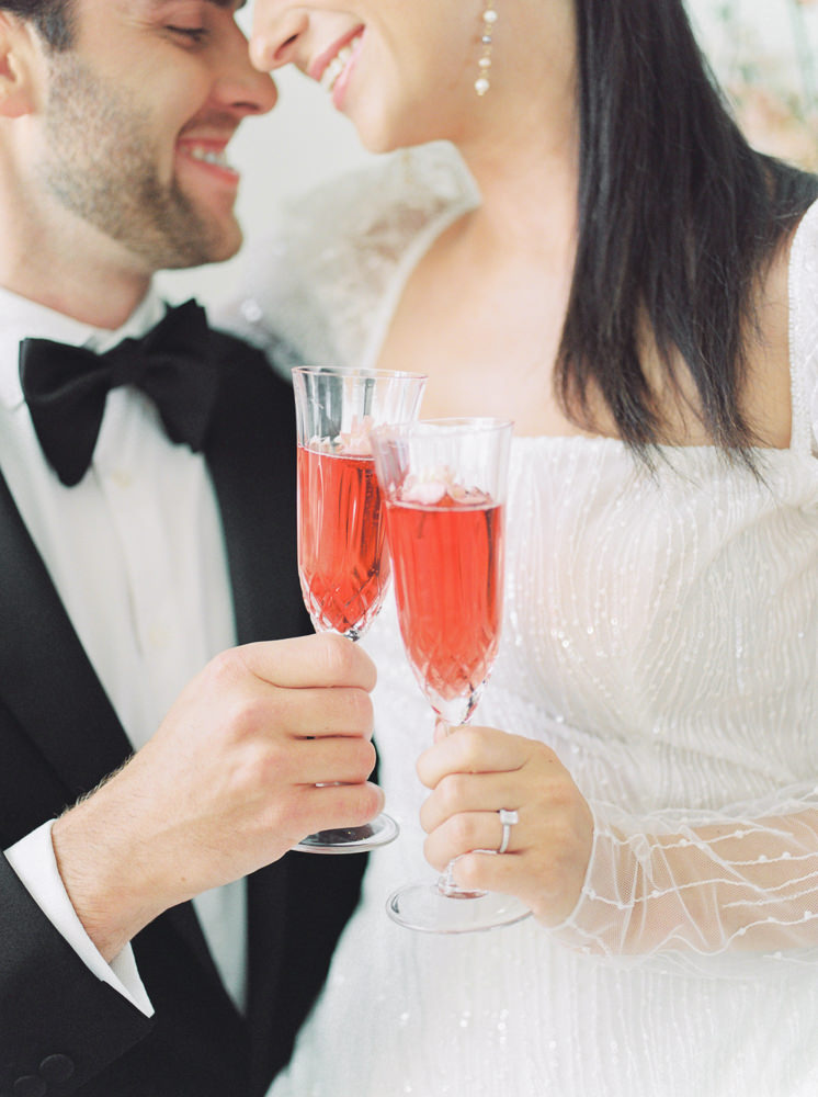 bride and groom nuzzle up closely with wide grins and they cheers with champagne on their wedding day