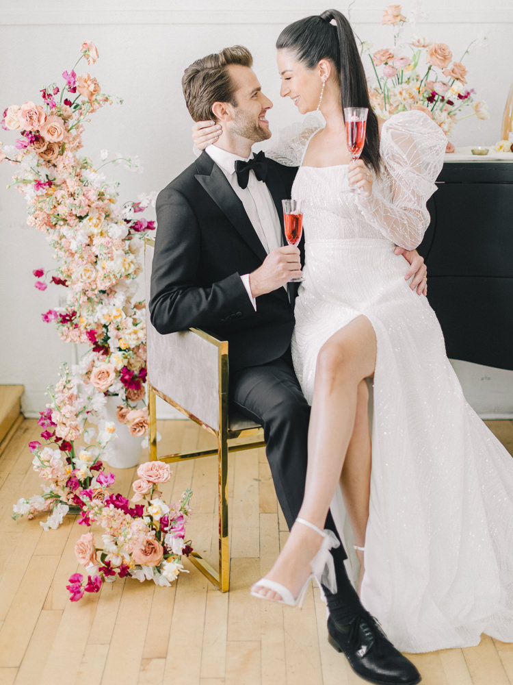Bride in a puffy-sleeved modern dress sits on her groom's lap for wedding photos