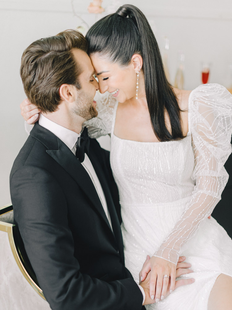 Bride sits on her groom's lap and touches her forehead to his lovingly