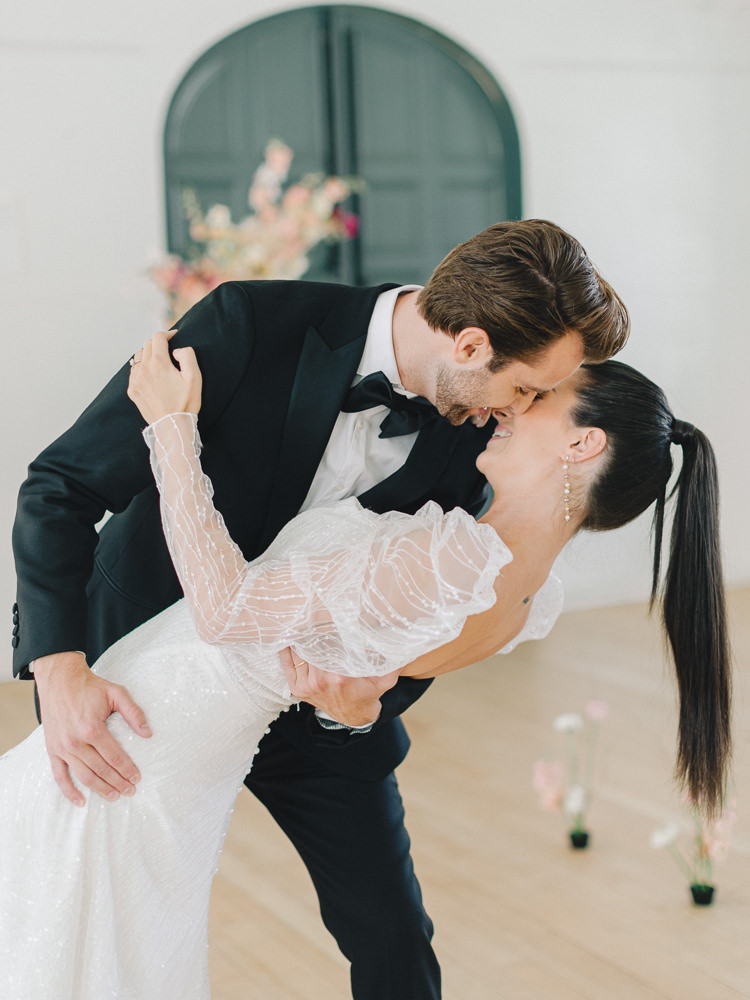 Groom wearing a tux dips his bride as she holds onto him smiling captured by their wedding film photographer