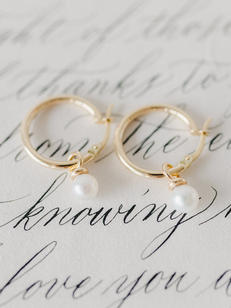 Delicate bridal earrings placed overtop paper with calligraphy 
