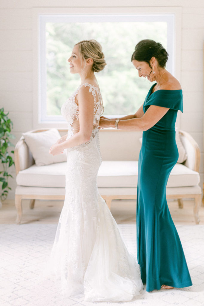 Bride has her dress buttoned by her mom while she gets ready for her wedding