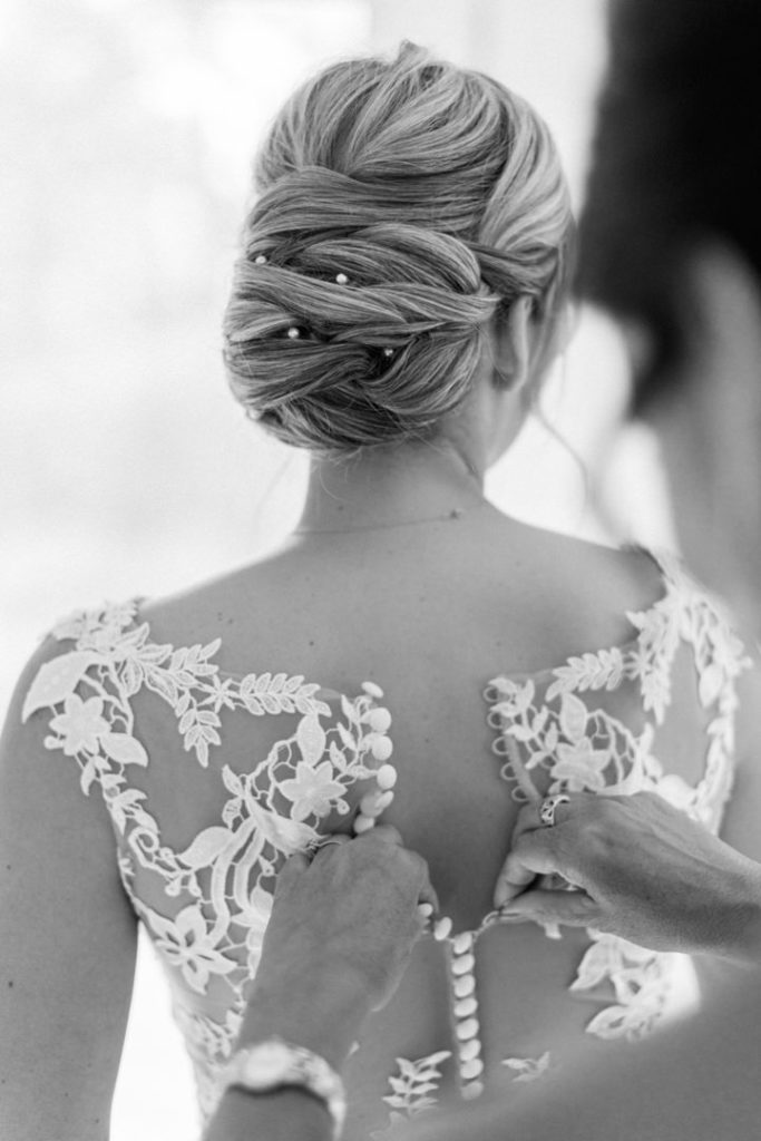Detail shot of the back of a bride's lace wedding dress as the final top buttons are clasped