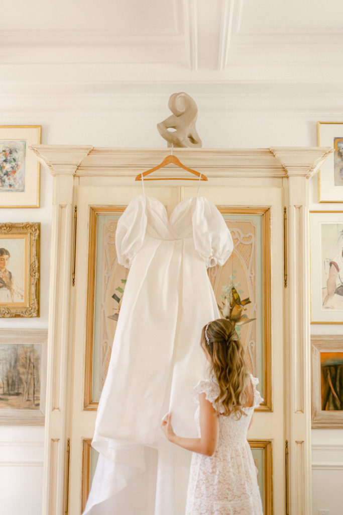 Bride admires her dress as it hangs in her getting ready space before she puts it on for her wedding