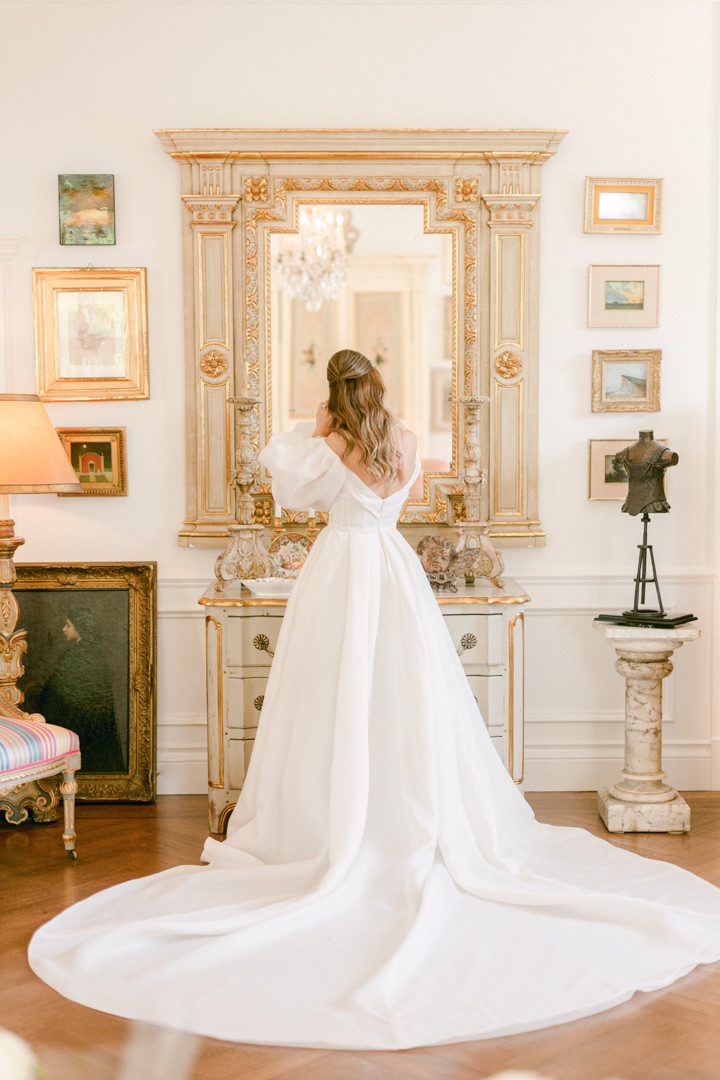 stunning bride stands in her wedding dress getting ready in front of a mirror