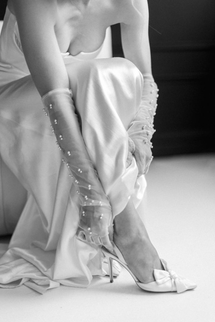 black and white photo of a bride putting on her shoes as she finishes getting ready for her wedding