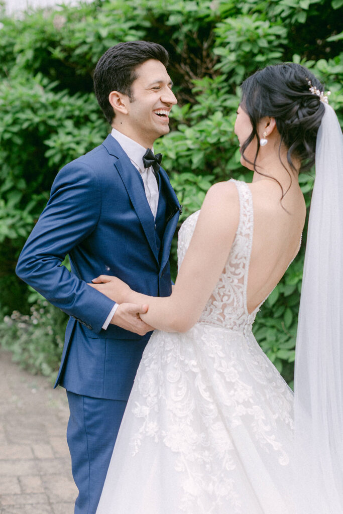 Groom in a blue suit shares a laugh with his bride during their first look before their wedding ceremony