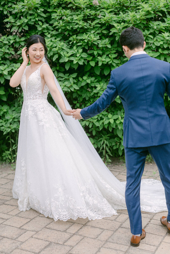 Bride shows off her stunning detailed wedding dress to her groom during their first look outdoors