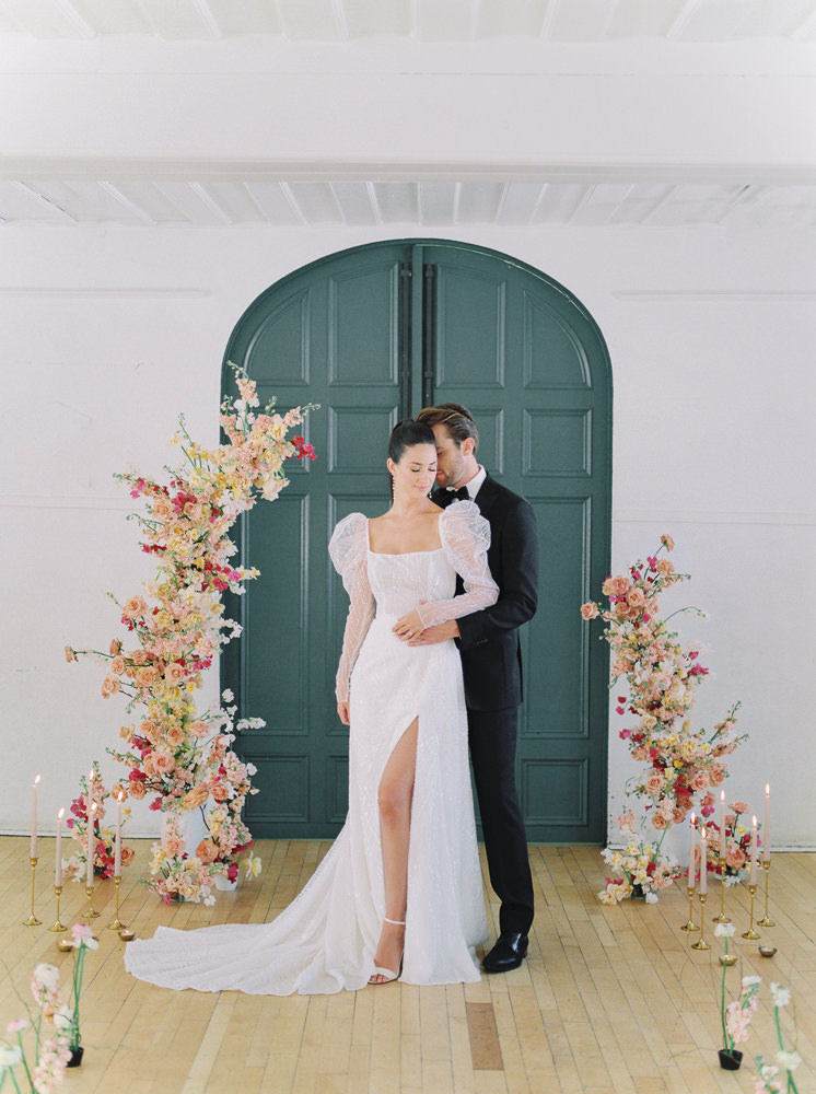 Bride and groom pose together in front of a floral arch for their modern wedding