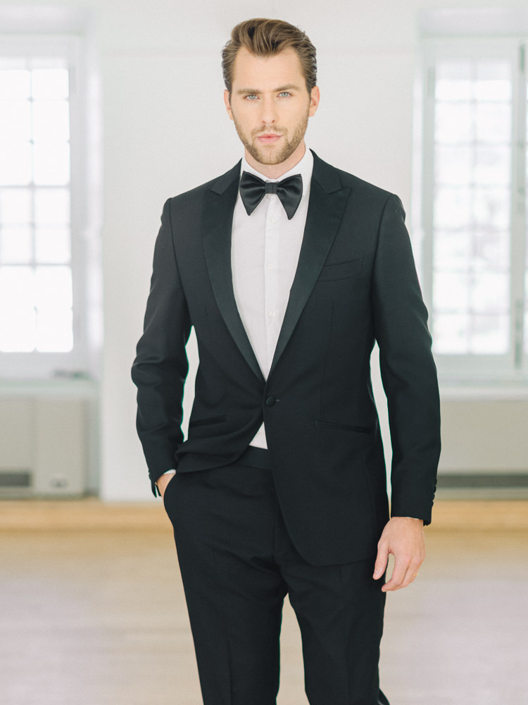 Groom gives the camera his best gaze while standing with one hand in the pocket of his tuxedo